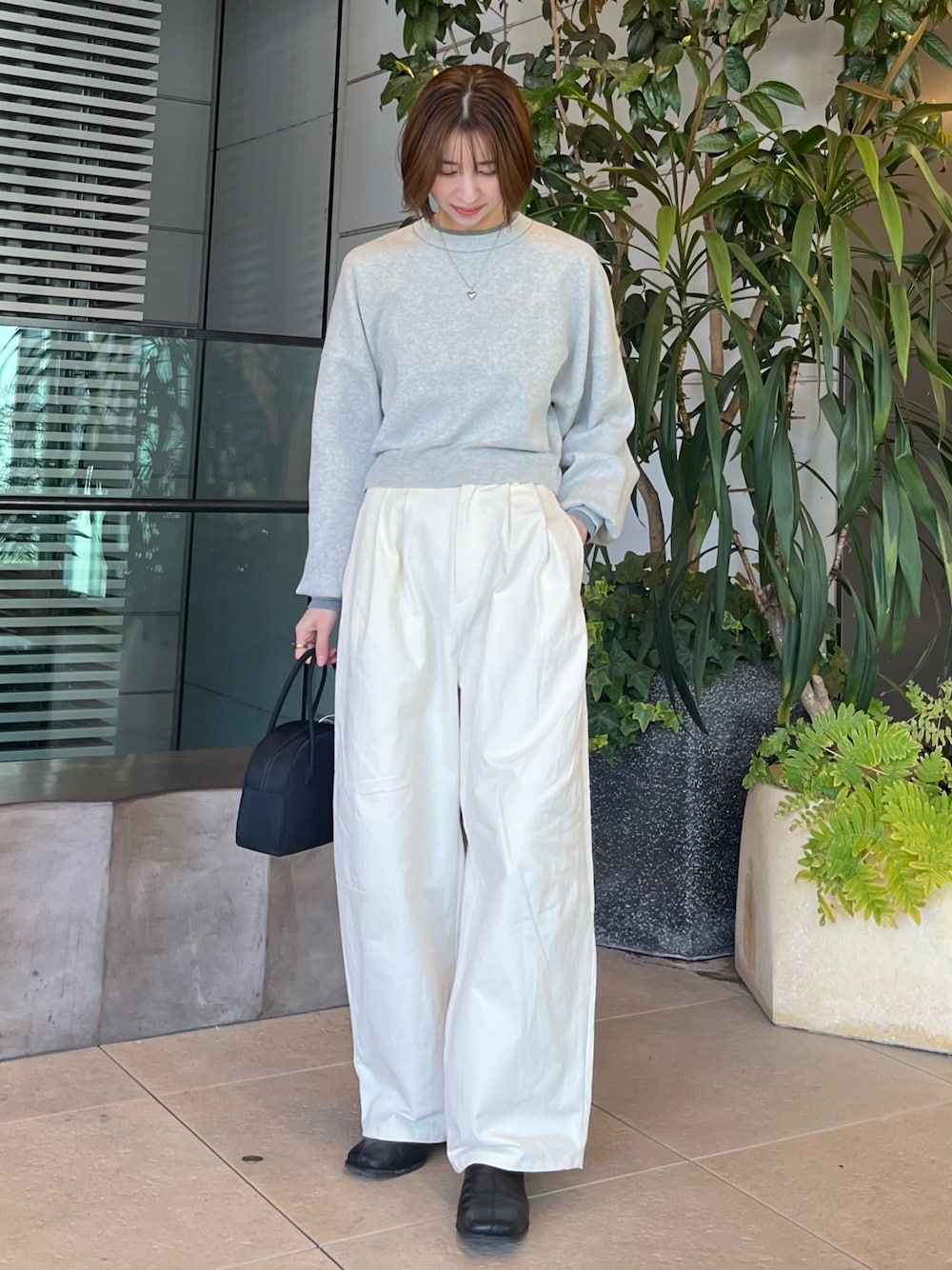 グレー系のニット/セーター、ホワイト系のチノパンツ、ブラック系のボストンバッグを着用したレディースの冬コーディネートの1枚目の写真