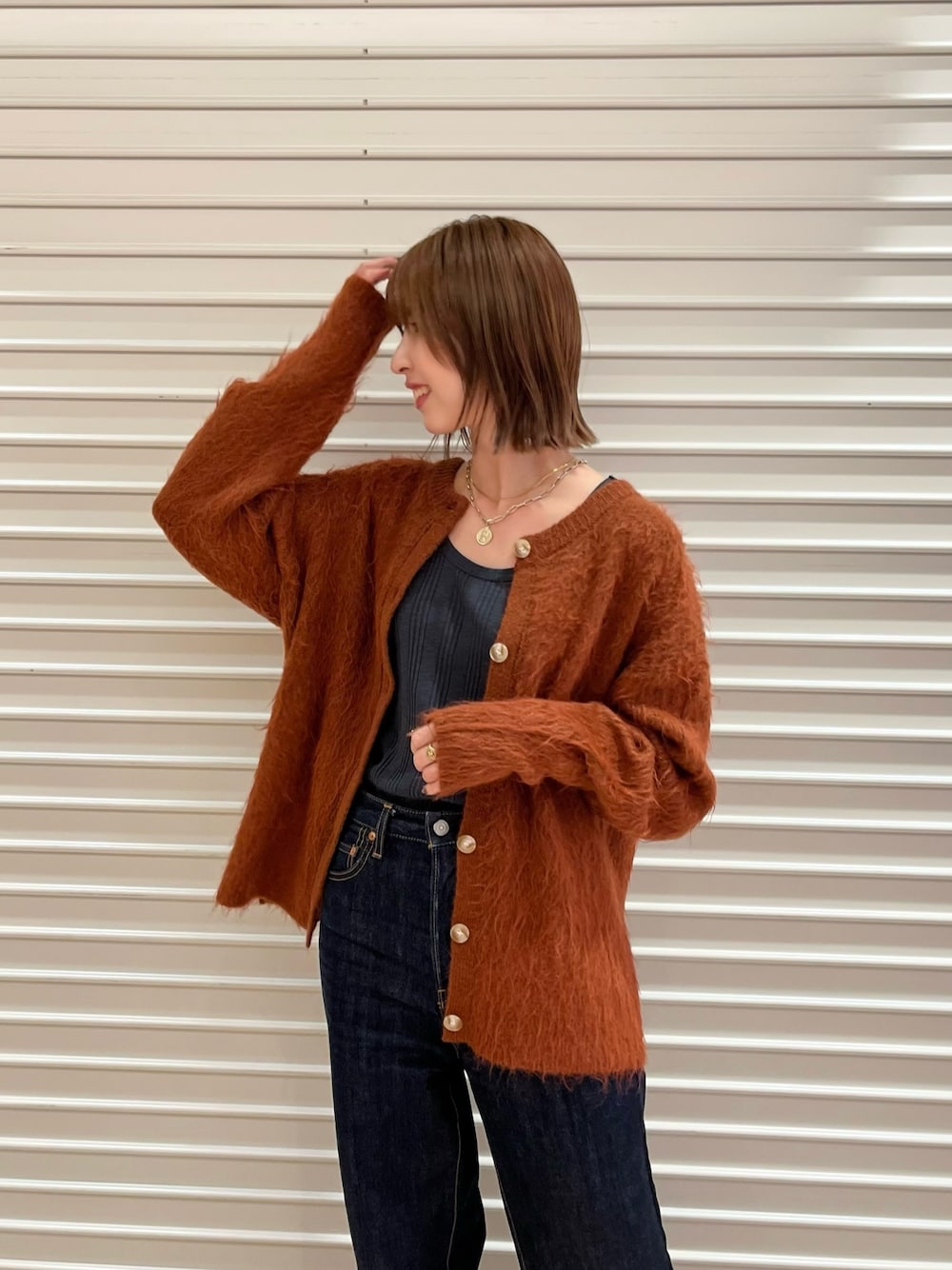 グレー系のTシャツ/カットソー、オレンジ系のカーディガン/ボレロ、ブルー系のデニムパンツを着用したレディースの秋コーディネートの1枚目の写真