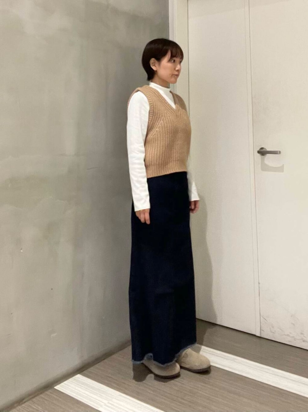 ベージュ系のベスト、ブルー系のスカート、ホワイト系のTシャツ/カットソーを着用したレディースの冬コーディネートの1枚目の写真