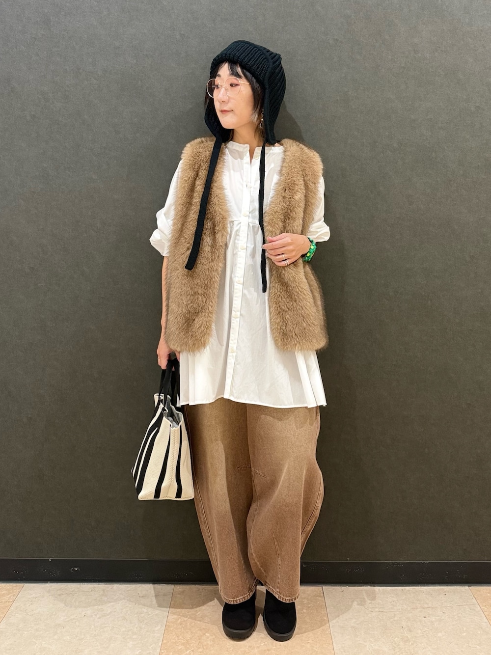 イエロー系のベスト、ホワイト系のチュニック、ブラウン系のデニムパンツを着用したレディースの秋コーディネートの1枚目の写真