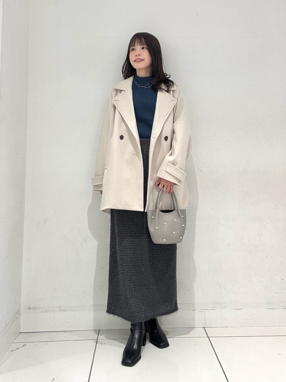 ブルー系のニット/セーター、ベージュ系のその他アウター、グレー系のスカートを着用したレディースの冬コーディネートの1枚目の写真