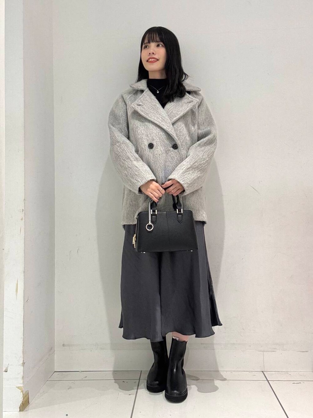 グレー系のスカート、ブラック系のブーツ、ブラック系のハンドバッグを着用したレディースの冬コーディネートの1枚目の写真