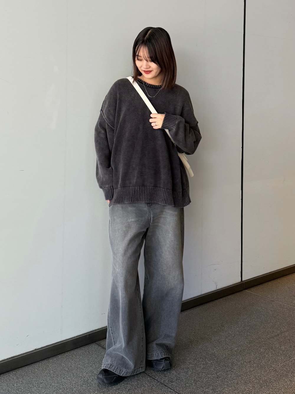 ブラック系のデニムパンツ、ブラック系のニット/セーター、ホワイト系のショルダーバッグを着用したレディースの秋コーディネートの1枚目の写真
