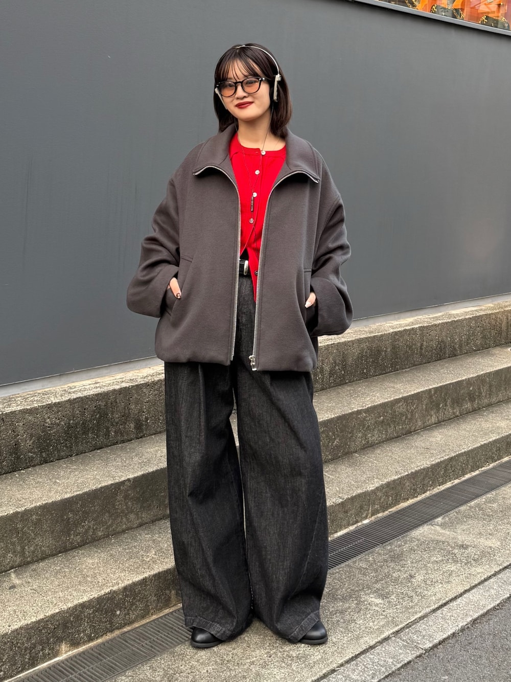 グレー系のブルゾン、レッド系のカーディガン/ボレロ、ブラック系のデニムパンツを着用したレディースの秋コーディネートの1枚目の写真