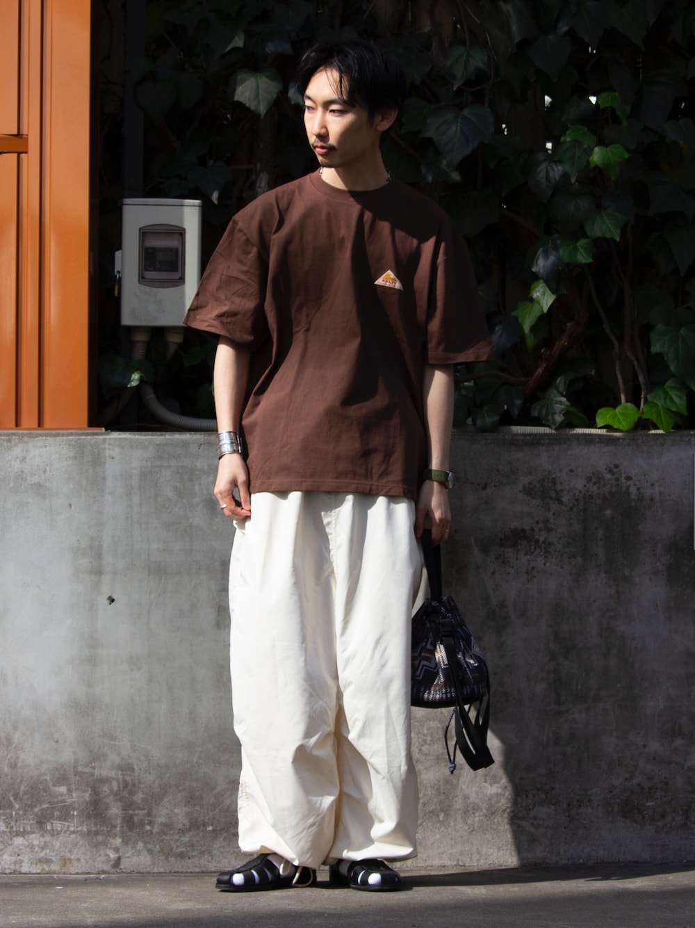 ブラウン系のTシャツ/カットソー、ホワイト系のその他パンツ、ブラック系のショルダーバッグを着用したメンズの春コーディネートの1枚目の写真