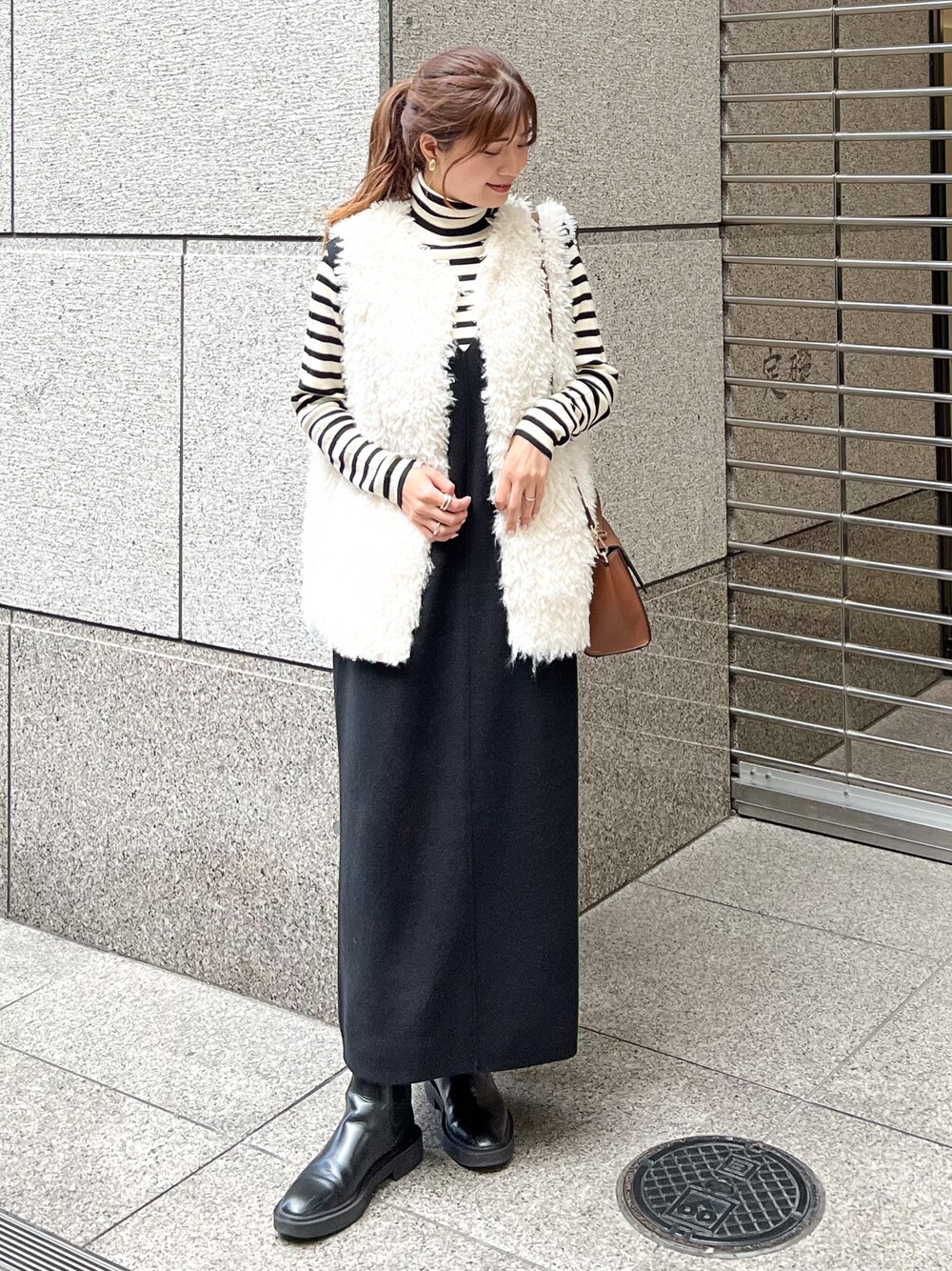 ブラック系のジャンパースカート、ホワイト系のニット/セーター、ホワイト系のベストを着用したレディースの秋コーディネートの1枚目の写真