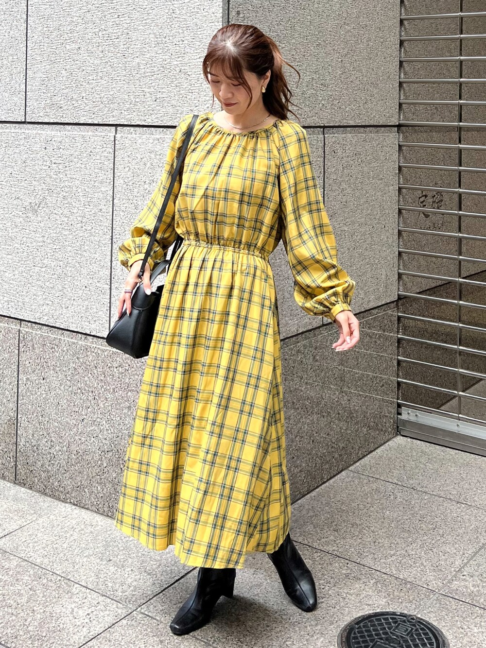イエロー系のワンピース、ブラック系のショルダーバッグ、ブラック系のブーツを着用したレディースの秋コーディネートの1枚目の写真