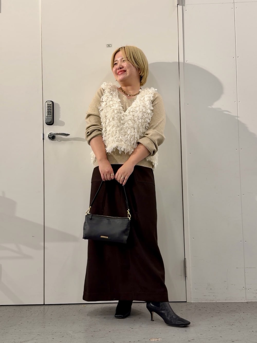 ホワイト系のベスト、ベージュ系のニット/セーター、ブラウン系のスカートを着用したレディースの冬コーディネートの1枚目の写真