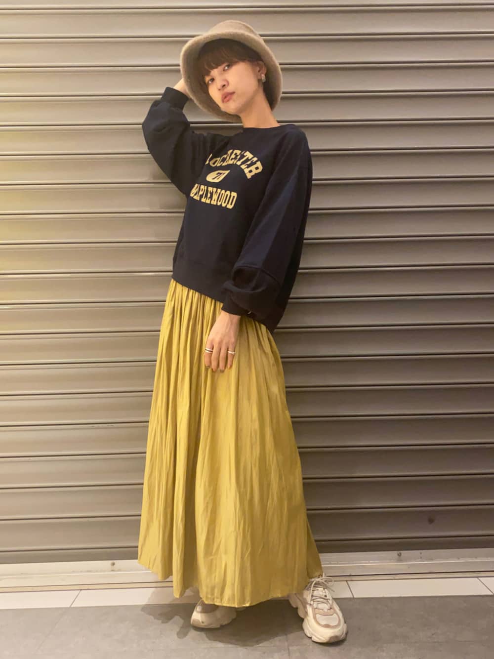 イエロー系のスカート、ブルー系のTシャツ/カットソー、ブラウン系のキャップを着用したレディースの秋コーディネートの1枚目の写真