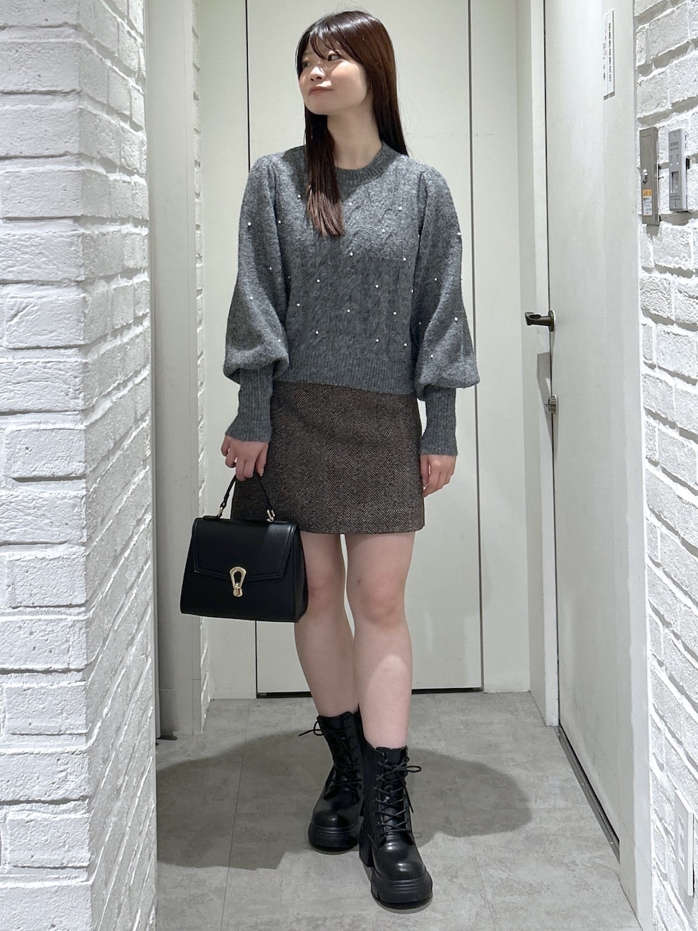 ブラック系のトートバッグ、ブラック系のブーツ、ブラウン系のスカートを着用したレディースの秋コーディネートの1枚目の写真