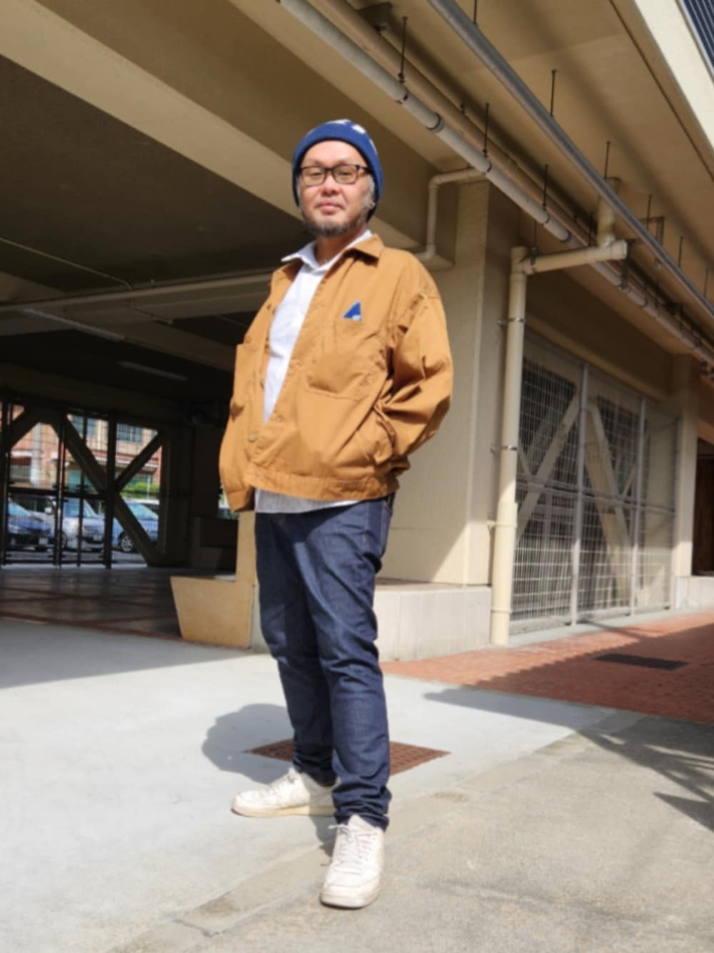 ブルー系のデニムパンツ、ホワイト系のスニーカー、ブラウン系のブルゾンを着用したメンズの春コーディネートの1枚目の写真