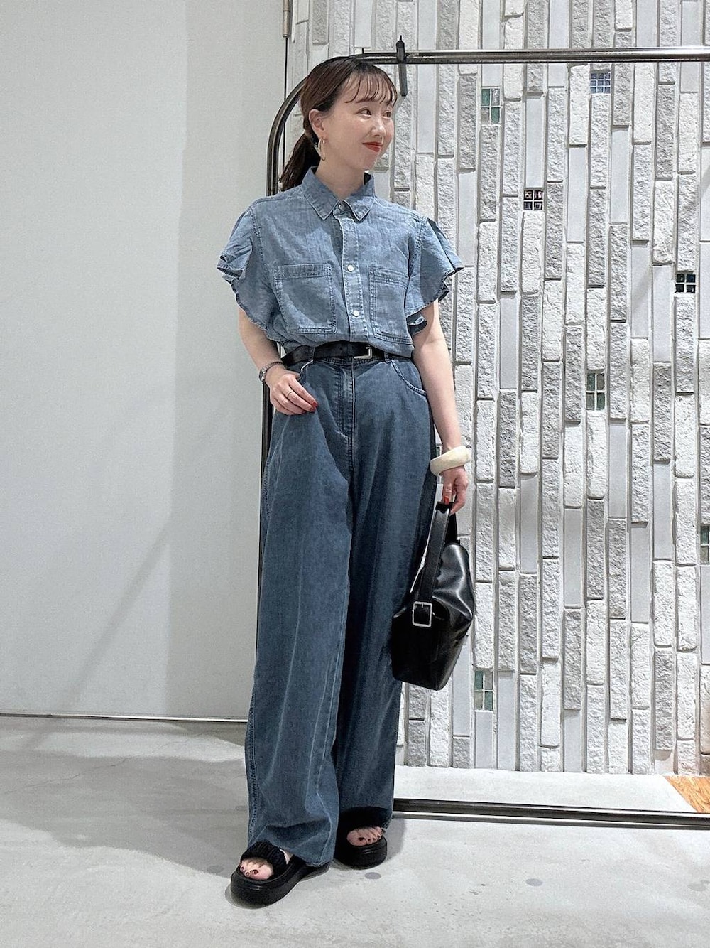 ブルー系のデニムパンツ、ブラック系のサンダル、ブラック系のショルダーバッグを着用したレディースの春コーディネートの1枚目の写真