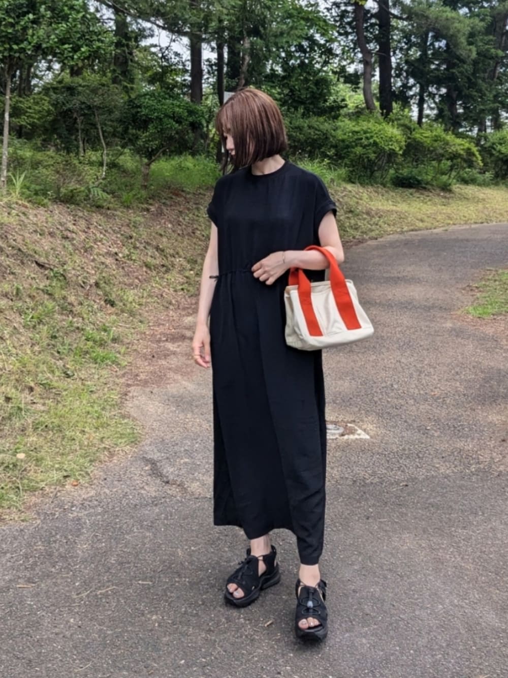 ブラック系のワンピース、オレンジ系のトートバッグ、ブラック系のサンダルを着用したレディースの夏コーディネートの1枚目の写真