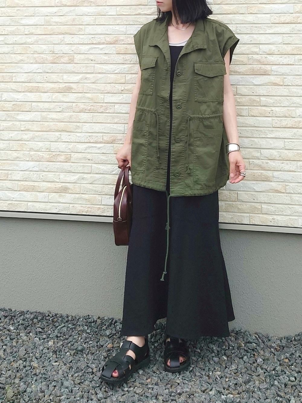 ブラック系のワンピース、グリーン系のベスト、ブラック系のサンダルを着用したレディースの夏コーディネートの1枚目の写真