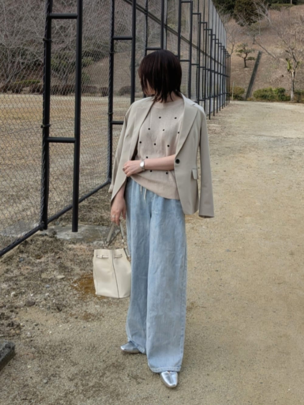 ベージュ系のニット/セーター、ブルー系のデニムパンツ、ホワイト系のショルダーバッグを着用したレディースの春コーディネートの1枚目の写真