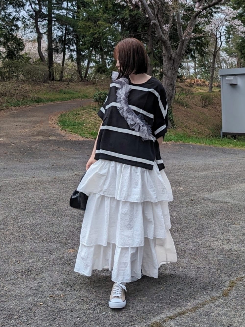 ブラック系のTシャツ/カットソー、ホワイト系のスカート、ベージュ系のスニーカーを着用したレディースの春コーディネートの1枚目の写真