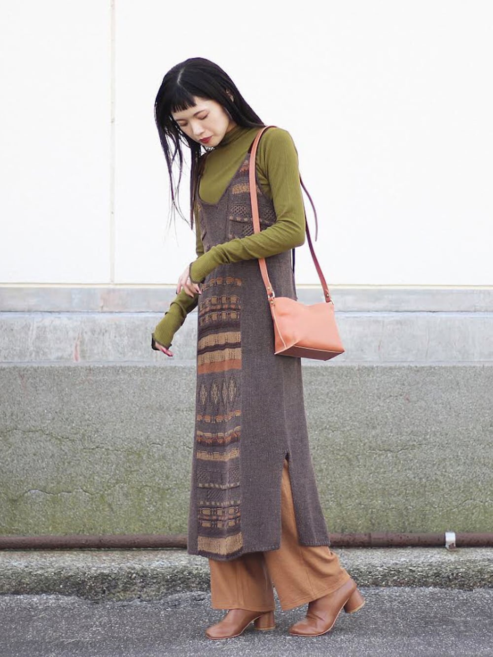 グリーン系のトップス、オレンジ系のショルダーバッグ、ブラウン系のワンピースを着用したレディースの秋コーディネートの1枚目の写真