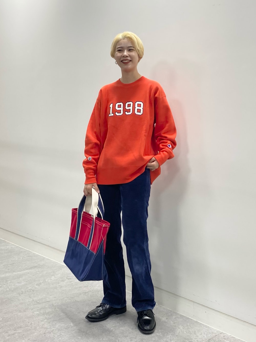 オレンジ系のスウェット、グリーン系のトートバッグ、ブラック系のドレスシューズを着用したレディースの秋コーディネートの1枚目の写真