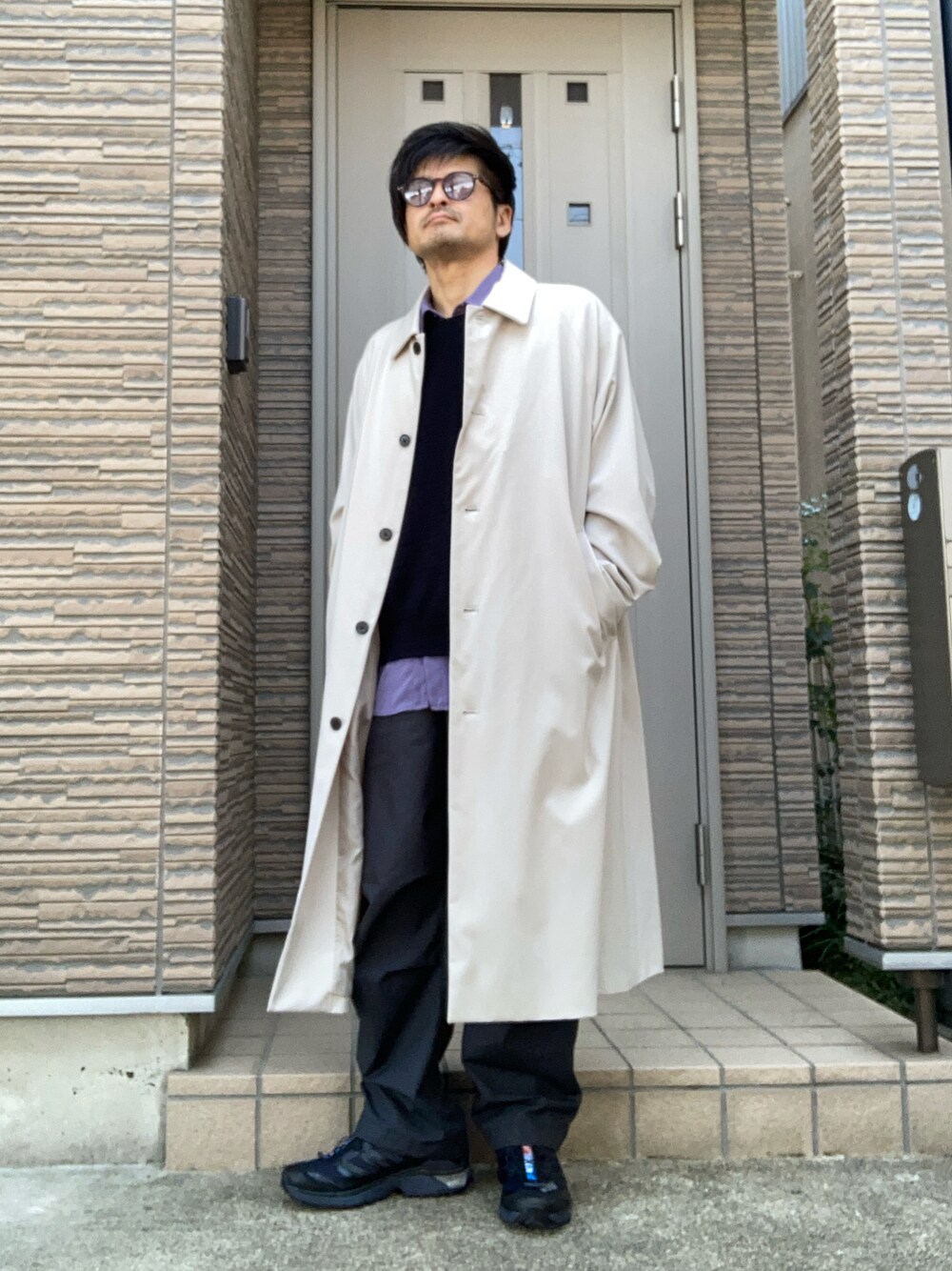 ベージュ系のステンカラーコート、グレー系のパンツ、ブラック系のスニーカーを着用したメンズの春コーディネートの1枚目の写真