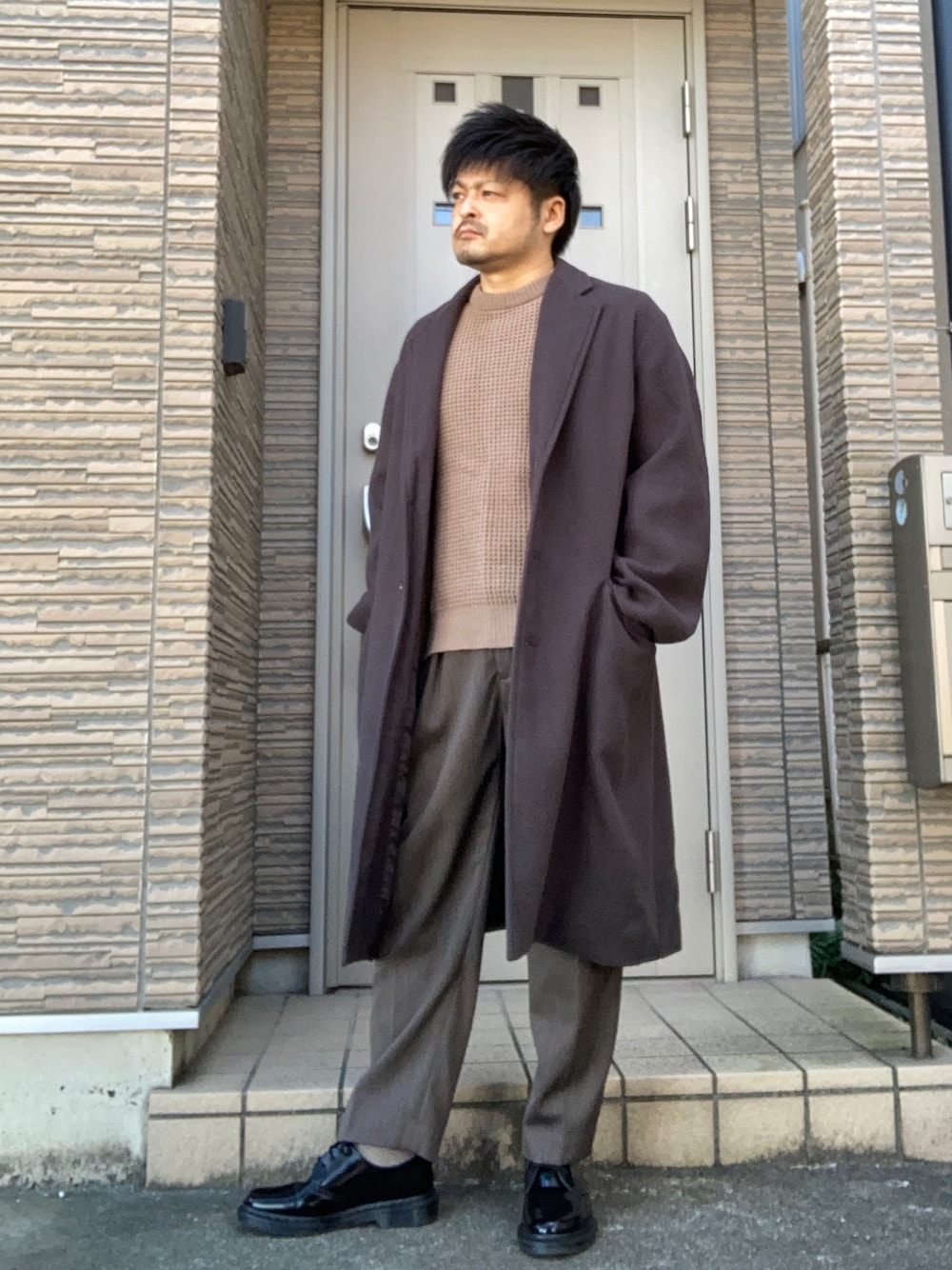 ブラウン系のスラックス、ブラック系のブーツ、グレー系のチェスターコートを着用したメンズの冬コーディネートの1枚目の写真