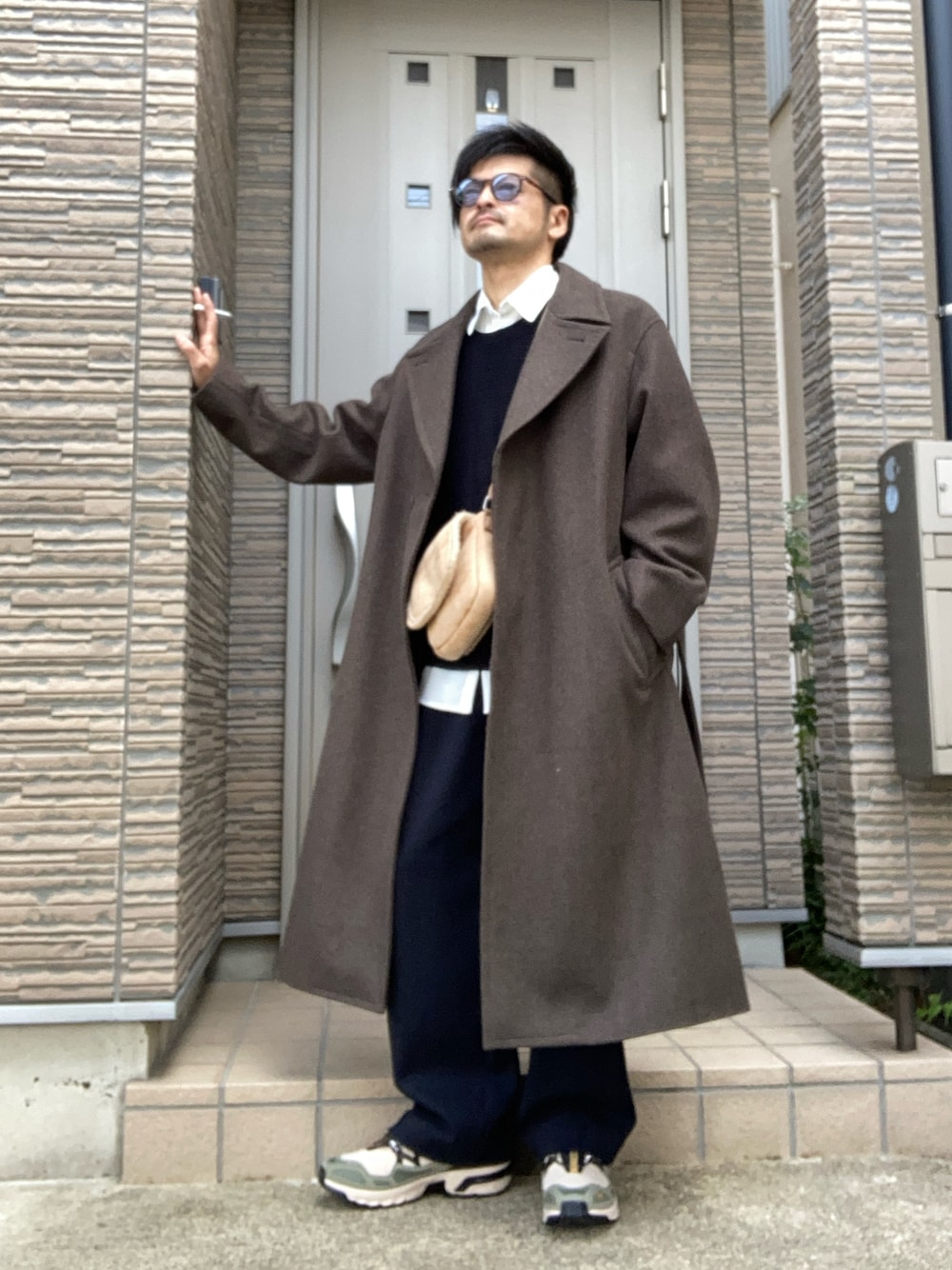 ベージュ系のスニーカー、ブラウン系のチェスターコート、イエロー系のショルダーバッグを着用したメンズの冬コーディネートの1枚目の写真