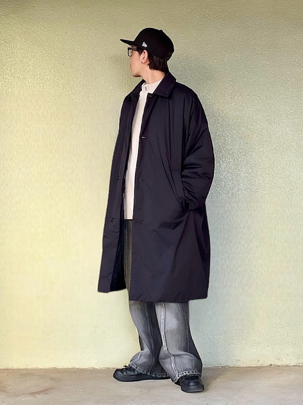 ブラック系のデニムパンツ、ブラック系のスニーカー、ブラック系のステンカラーコートを着用したメンズの冬コーディネートの1枚目の写真
