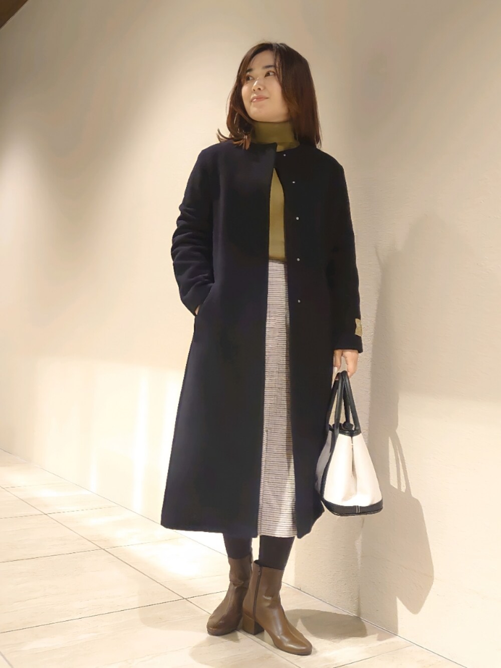 ブラック系のトートバッグ、イエロー系のブーツ、ホワイト系のスカートを着用したレディースの冬コーディネートの1枚目の写真