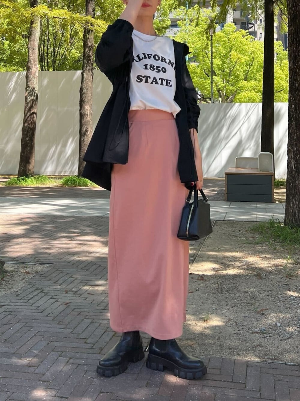 ブラック系のハンドバッグ、ブラック系のパーカー、ピンク系のスカートを着用したレディースの秋コーディネートの1枚目の写真