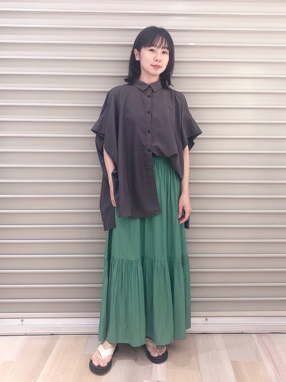 ブラック系のシャツ/ブラウス、グリーン系のスカート、ホワイト系のサンダルを着用したレディースの夏コーディネートの1枚目の写真