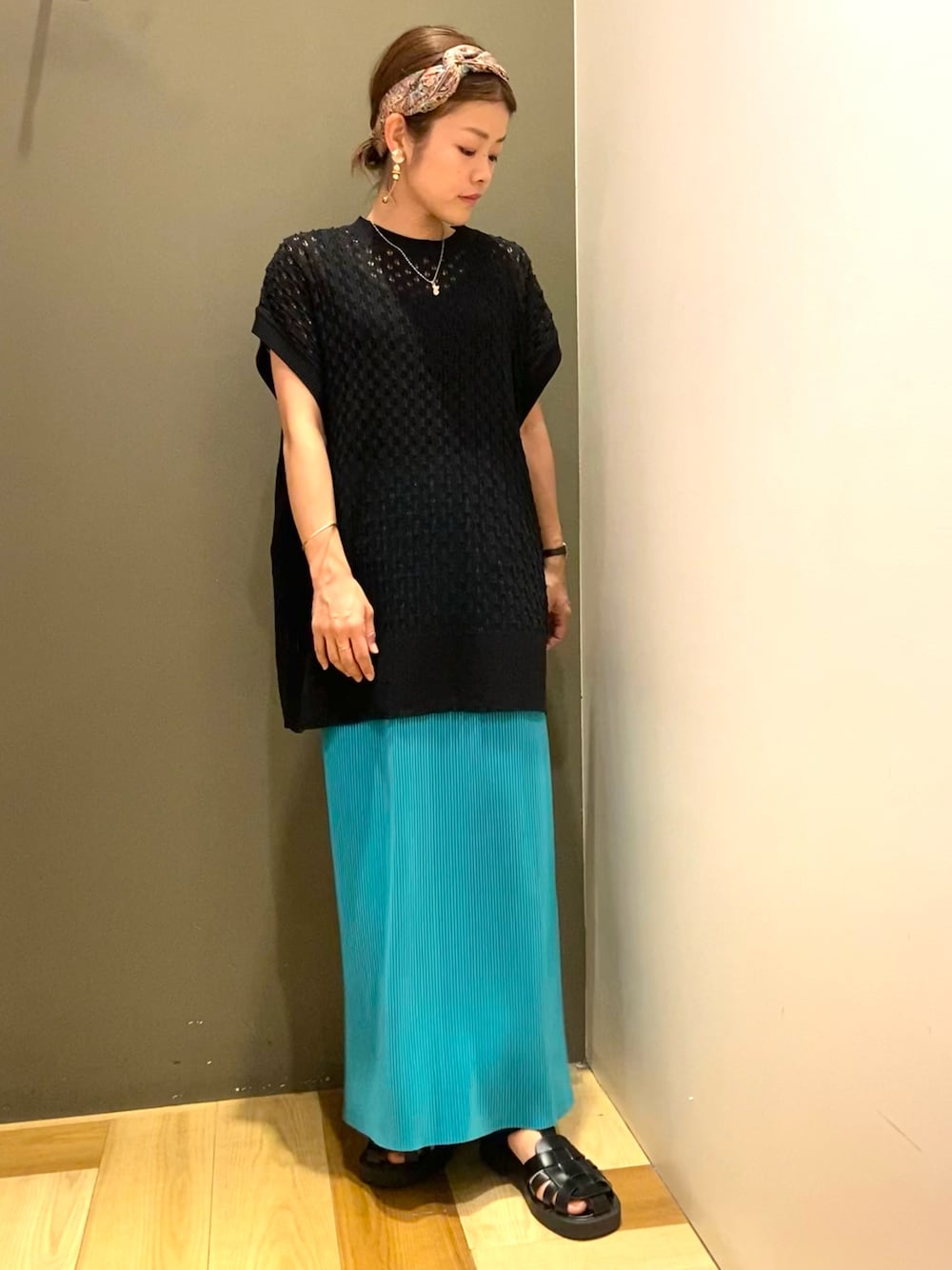 ブラック系のベスト、グリーン系のスカート、ブラック系のサンダルを着用したレディースの夏コーディネートの1枚目の写真