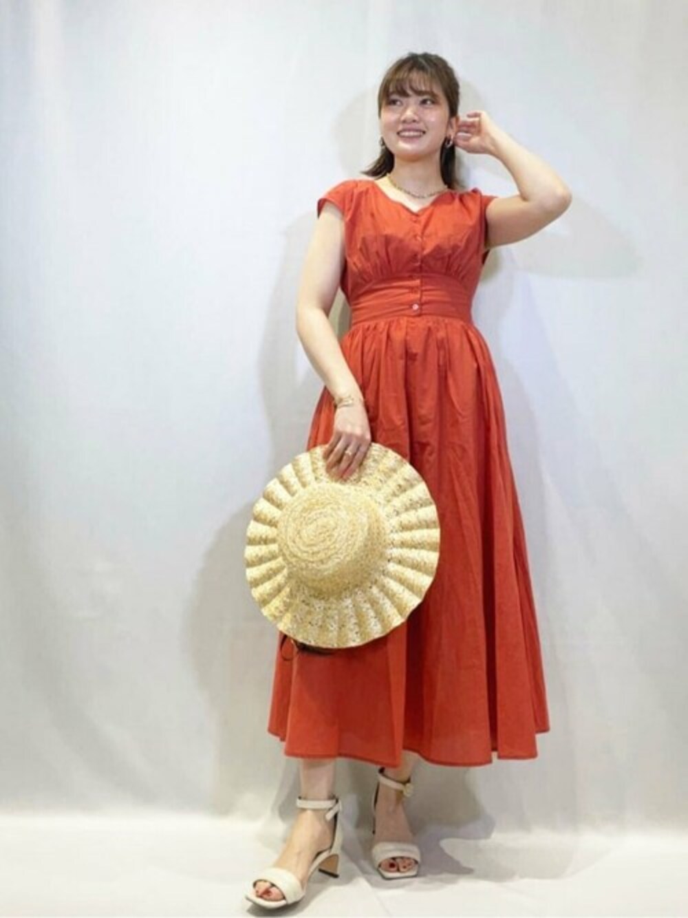 レッド系のワンピース、ホワイト系のサンダル、ベージュ系のハットを着用したレディースの春コーディネートの1枚目の写真