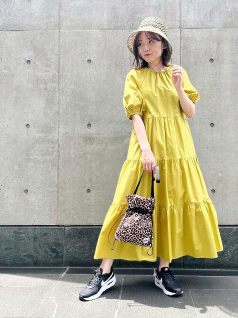 イエロー系のワンピース、ブラウン系のショルダーバッグ、ベージュ系のハットを着用したレディースの春コーディネートの1枚目の写真