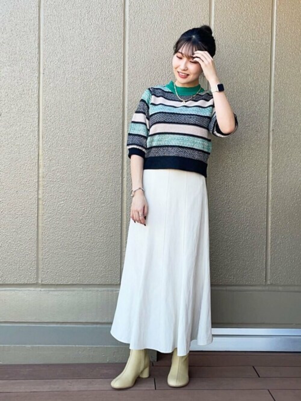 グリーン系のニット/セーター、ベージュ系のスカート、ベージュ系のブーツを着用したレディースの秋コーディネートの1枚目の写真
