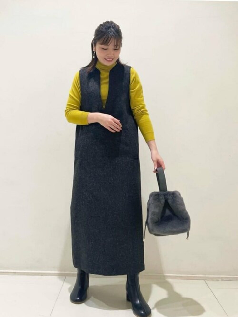 ブラック系のジャンパースカート、イエロー系のニット/セーター、ブラック系のブーツを着用したレディースの秋コーディネートの1枚目の写真