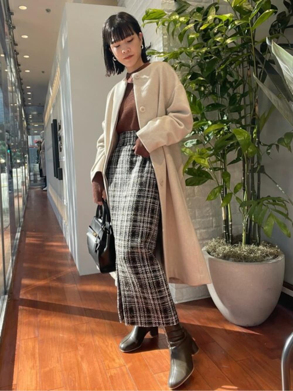 ブラウン系のニット/セーター、ホワイト系のノーカラーコート、ベージュ系のスカートを着用したレディースの冬コーディネートの1枚目の写真