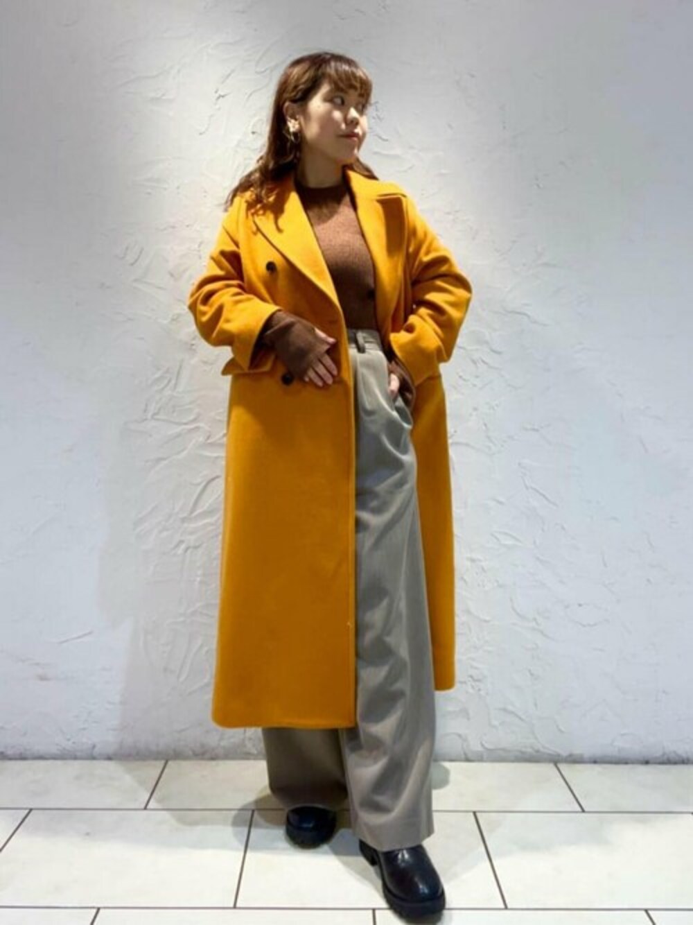 ブラウン系のニット/セーター、オレンジ系のチェスターコート、ブラウン系のその他パンツを着用したレディースの冬コーディネートの1枚目の写真