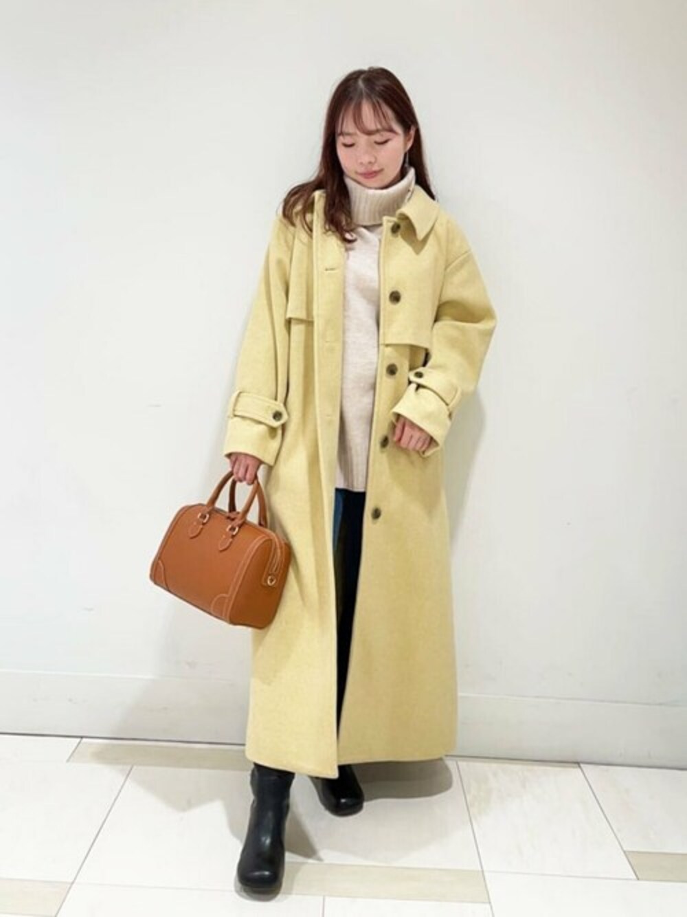 ベージュ系のニット/セーター、イエロー系のステンカラーコート、イエロー系のボストンバッグを着用したレディースの冬コーディネートの1枚目の写真