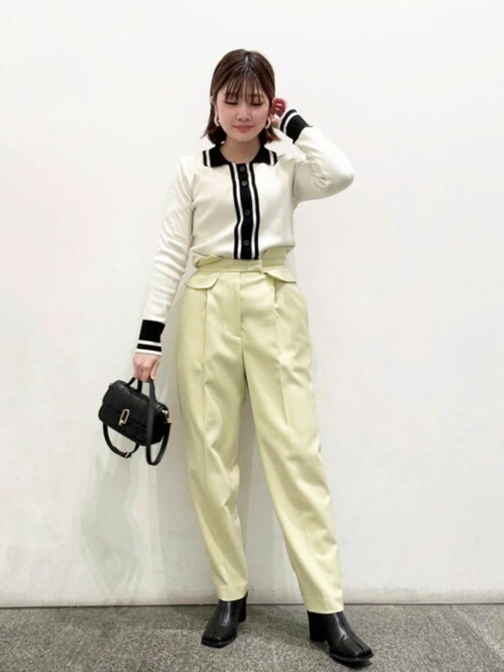 イエロー系のスラックス、ブラック系のショルダーバッグ、ホワイト系のニット/セーターを着用したレディースの冬コーディネートの1枚目の写真