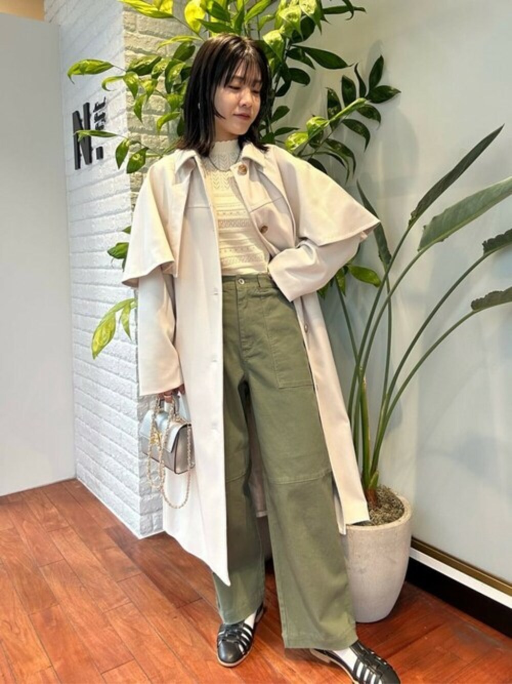 ホワイト系のトレンチコート、ベージュ系のニット/セーター、グリーン系のスラックスを着用したレディースの春コーディネートの1枚目の写真