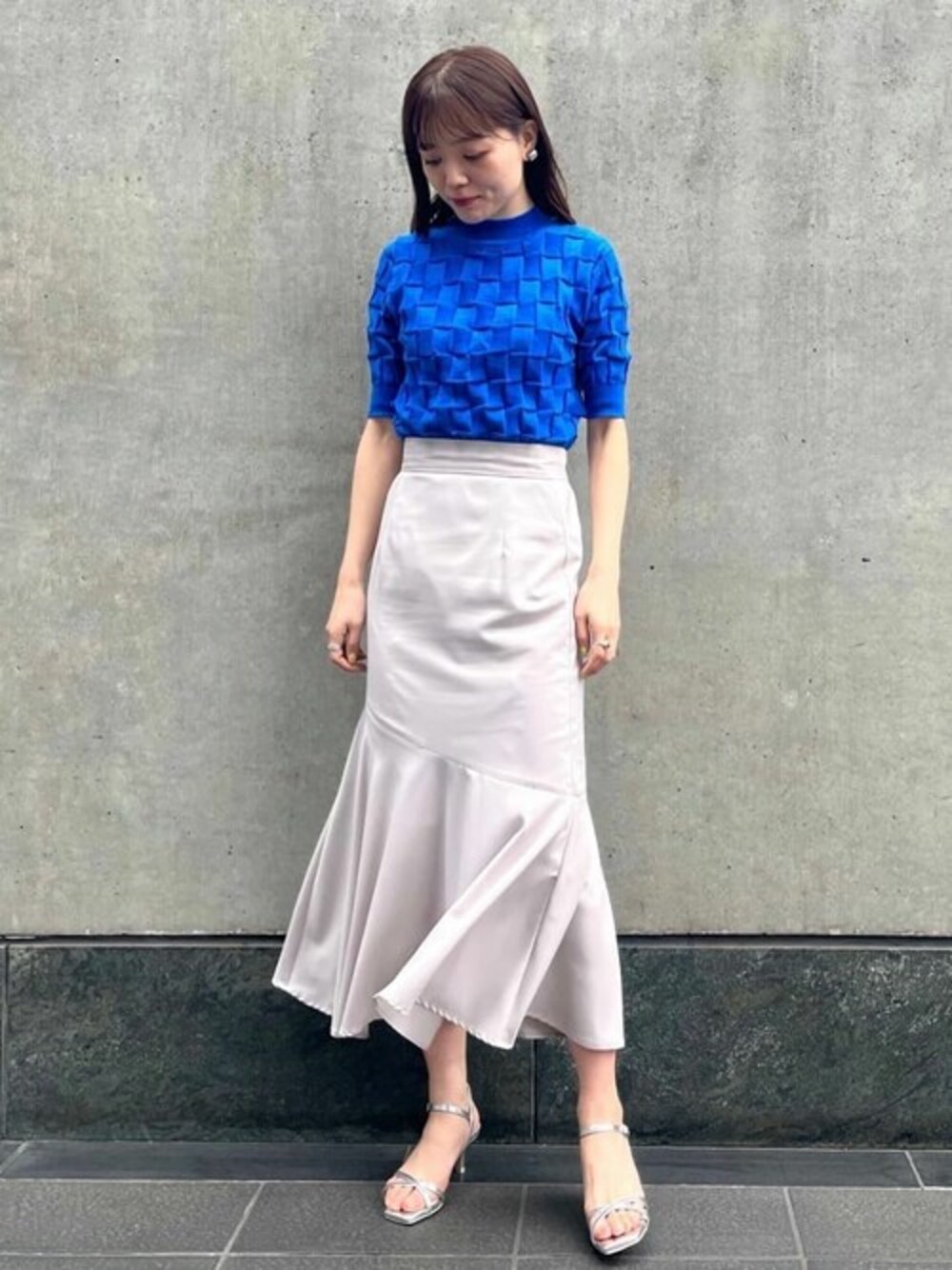 グレー系のスカート、ブルー系のニット/セーター、シルバー系のサンダルを着用したレディースの春コーディネートの1枚目の写真