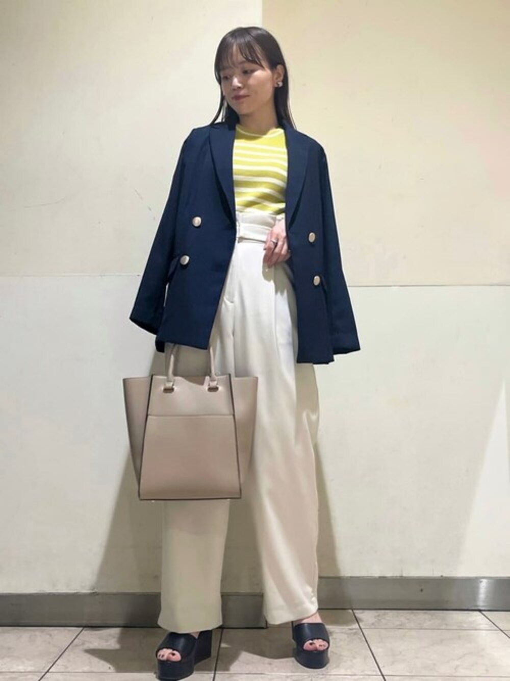 イエロー系のニット/セーター、ベージュ系のスラックス、ブルー系のテーラードジャケットを着用したレディースの春コーディネートの1枚目の写真