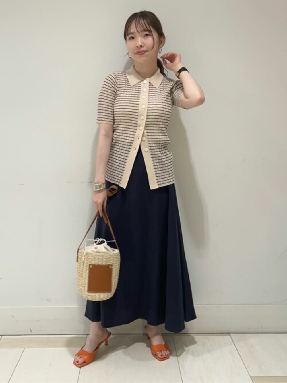 ブラック系のニット/セーター、オレンジ系のサンダル、ブルー系のスカートを着用したレディースの春コーディネートの1枚目の写真