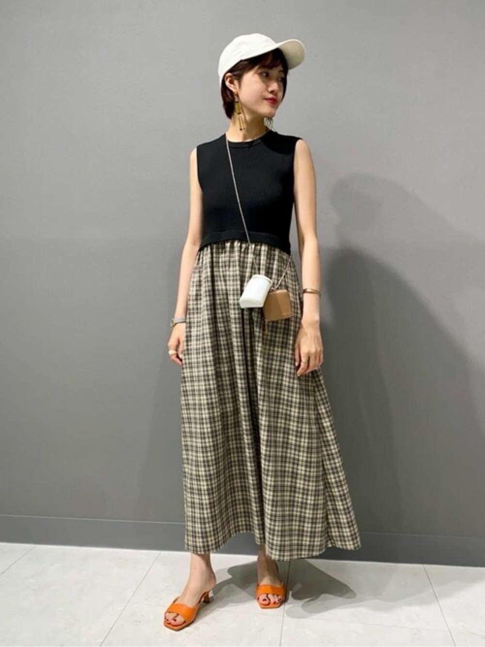 ブラック系のワンピース、オレンジ系のサンダル、ホワイト系のトートバッグを着用したレディースの夏コーディネートの1枚目の写真