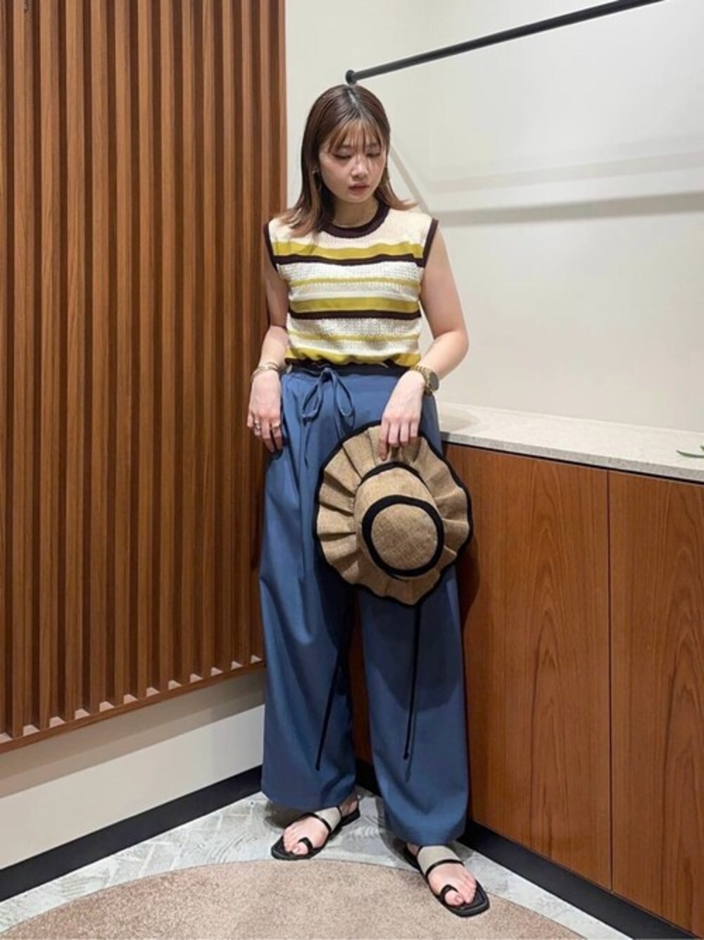 イエロー系のニット/セーター、ブルー系のスラックス、ゴールド系のネックレスを着用したレディースの夏コーディネートの1枚目の写真