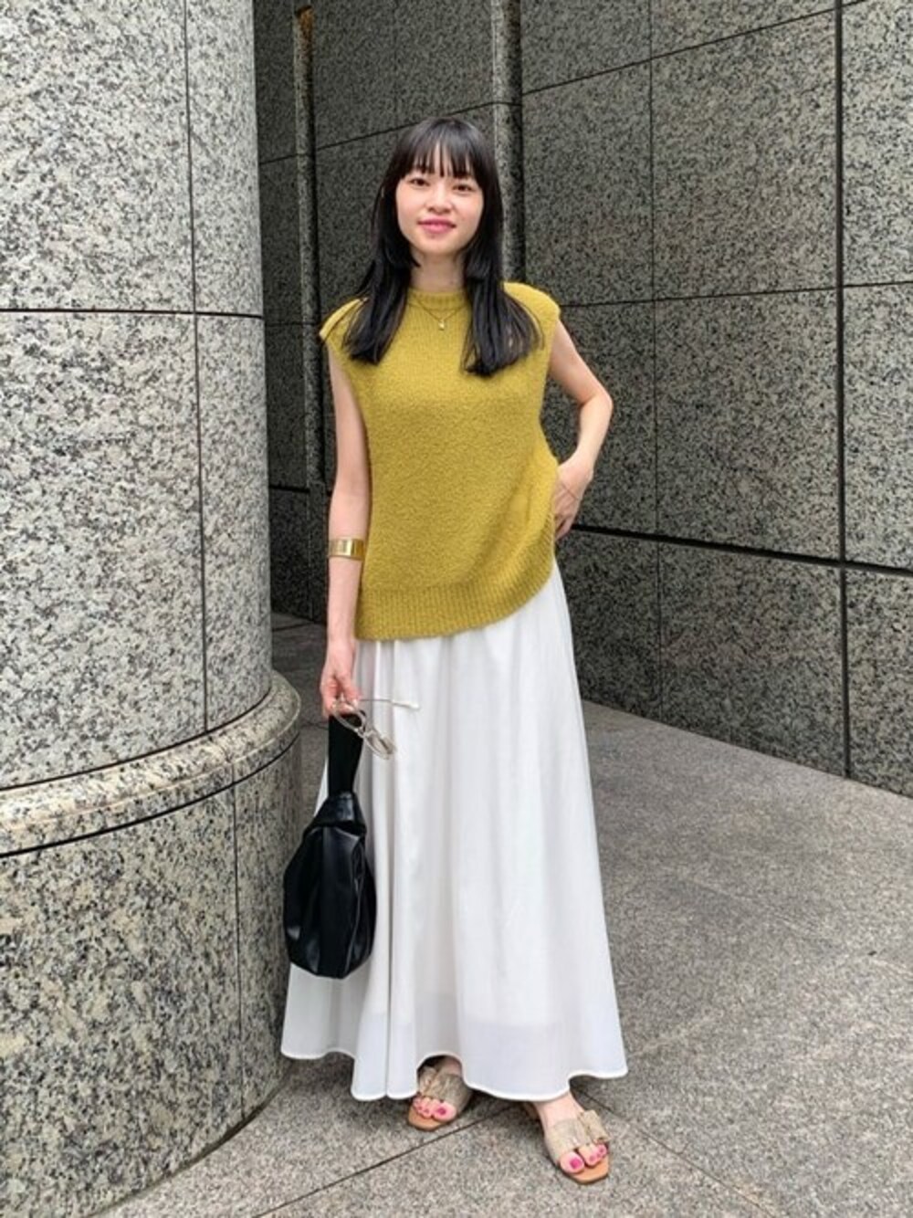 イエロー系のニット/セーター、ホワイト系のスカート、ブラック系のビジネスバッグを着用したレディースの夏コーディネートの1枚目の写真