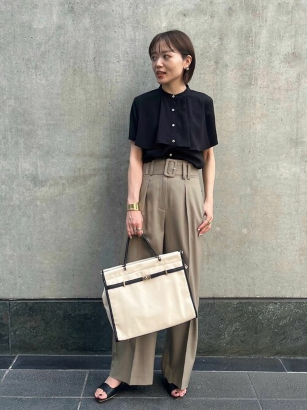 ベージュ系のスラックス、ブラック系のサンダル、ブラック系のシャツ/ブラウスを着用したレディースの夏コーディネートの1枚目の写真