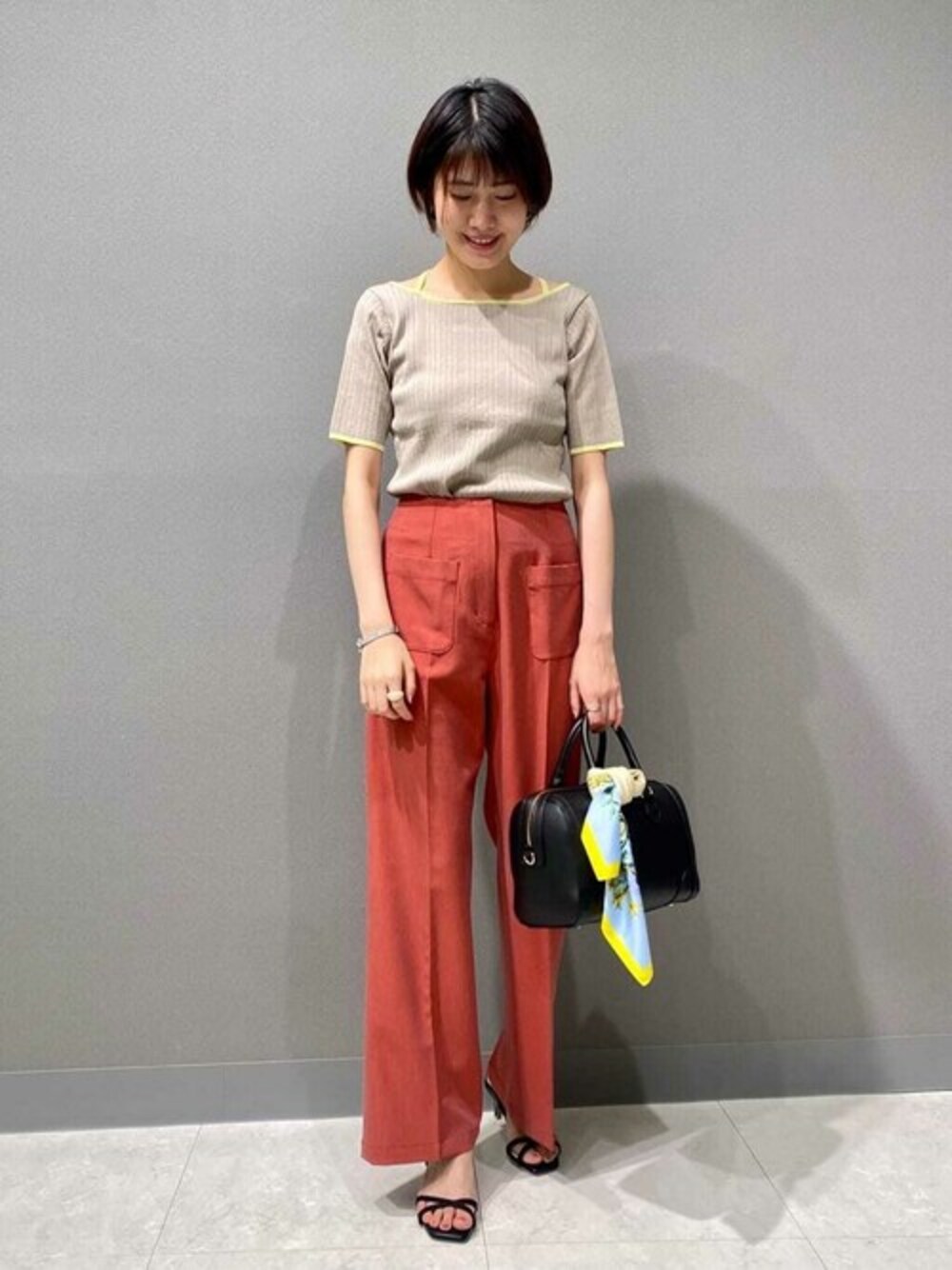 レッド系のスラックス、ベージュ系のニット/セーター、ブラック系のトートバッグを着用したレディースの夏コーディネートの1枚目の写真