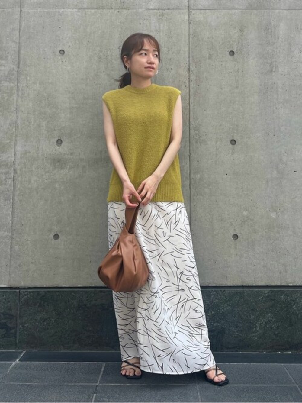 イエロー系のニット/セーター、ホワイト系のスカート、ベージュ系のビジネスバッグを着用したレディースの夏コーディネートの1枚目の写真