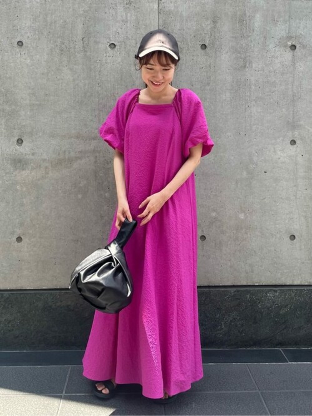 ピンク系のワンピース、ブラック系のビジネスバッグ、ブラック系のキャップを着用したレディースの夏コーディネートの1枚目の写真