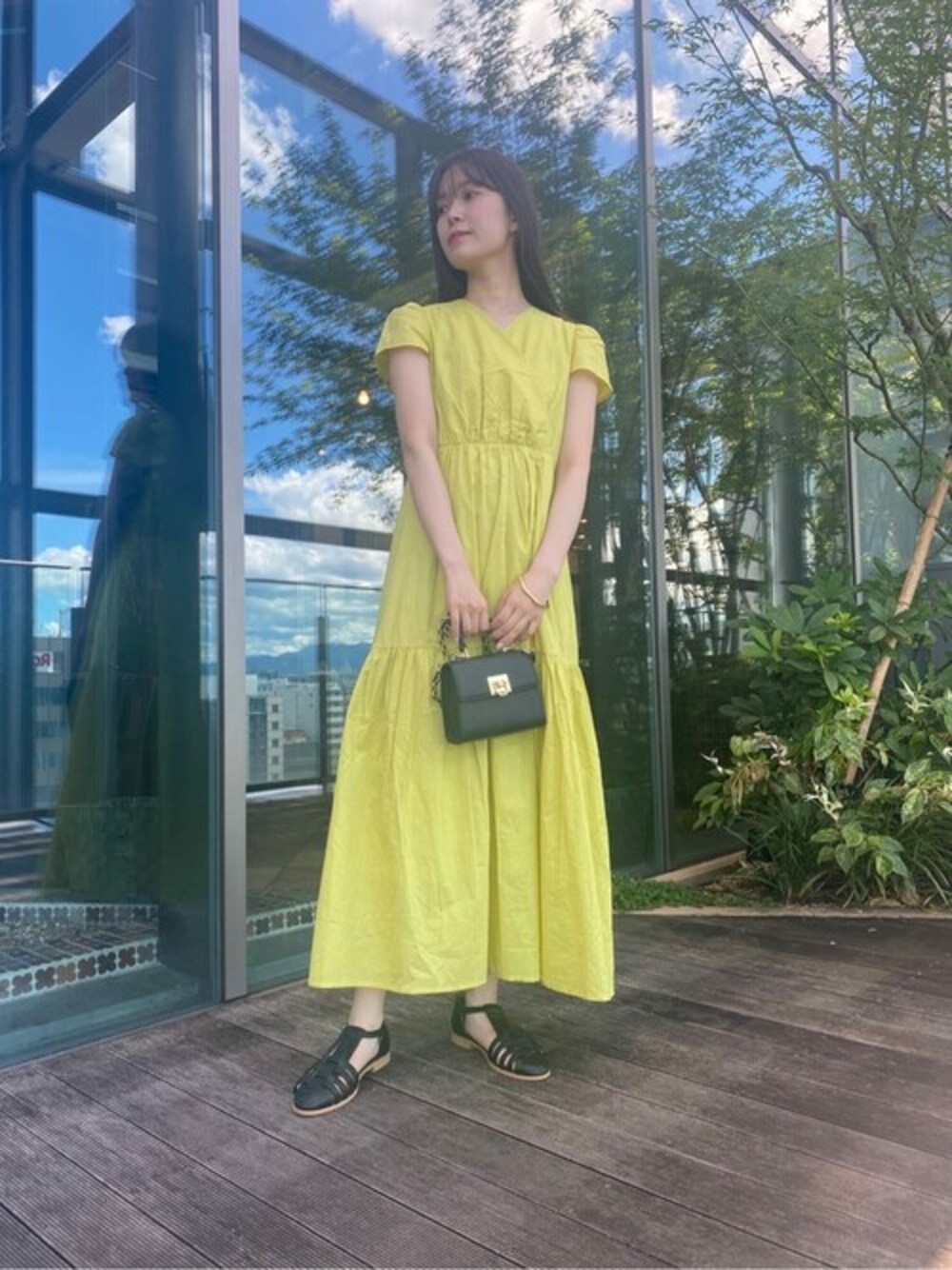 イエロー系のワンピース、ブラック系のショルダーバッグ、ブラック系のサンダルを着用したレディースの夏コーディネートの1枚目の写真